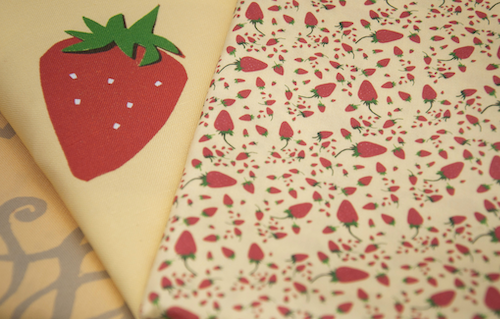 A close up of a Sally Harmon design of a strawberry on the left with a design with smaller ditsy strawberries on the right.