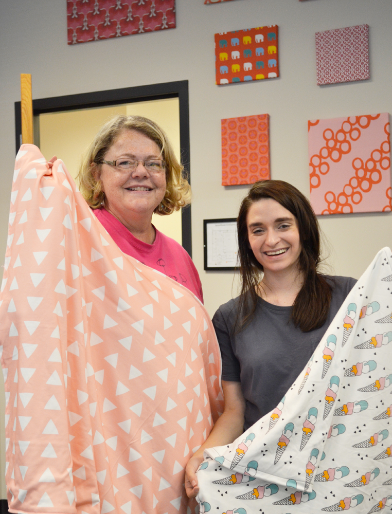 Spoonflower employees Erica and Jennifer share off the blankets they made in the top photo. Erica stands to the left with a pink blanket with rows of white triangles. Jennifer stands to the right holding a blanket with a white background featuring rows of ice cream cones, each with four scoops of ice cream, one orange, one lavender, one white and one light blue. The bottom photo shows Holly holding a handmade blanket that is white with rows of small black Xs. 