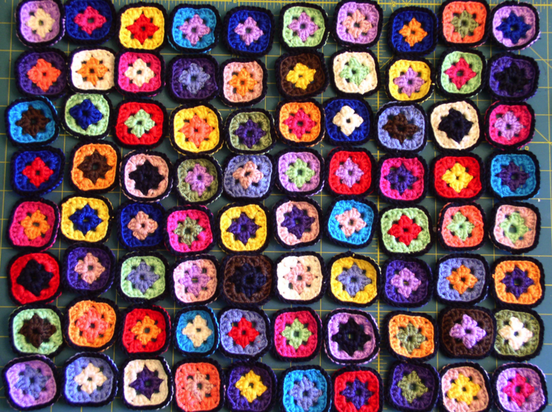 A photo of 10 rows of 8 crocheted granny squares laid out on a blue table. 
