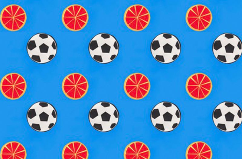 Fabric design with a bright blue background and alternating rows of black-and-white soccer balls and round orange slices. 
