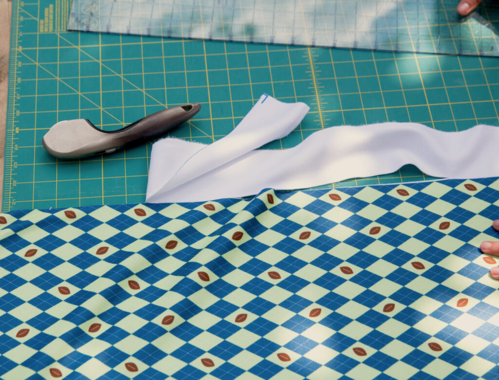 fleece fabric with green and blue argyle pattern on a green cutting mat next to a silver rotary cutter and acrylic quilting ruler. 