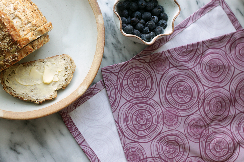 plate with bread and butter, bowl of blueberries and a napkin with a purple onion design on it, all sitting on a marble table