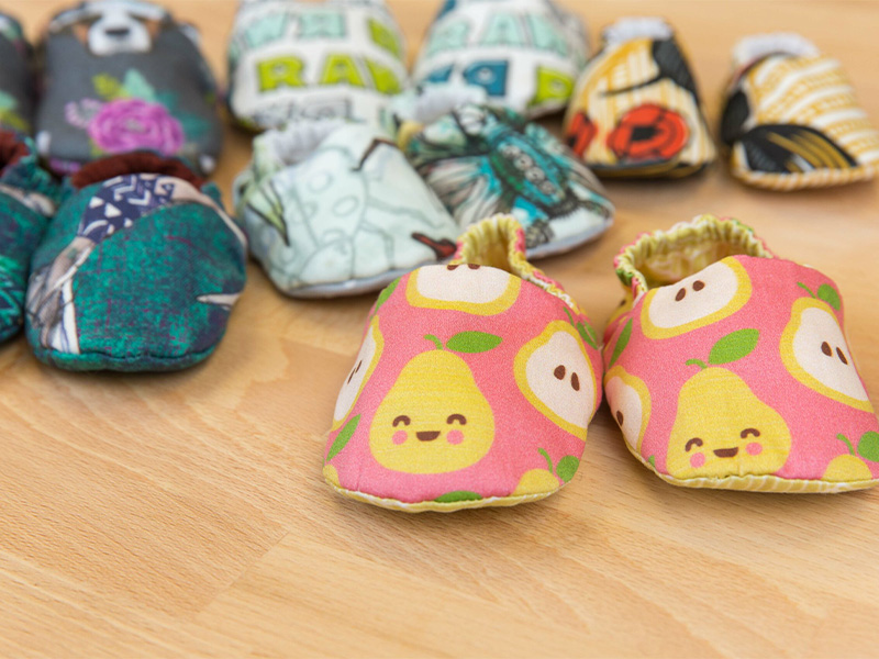 Pairs of fabric baby shoes sit on a wooden surface.