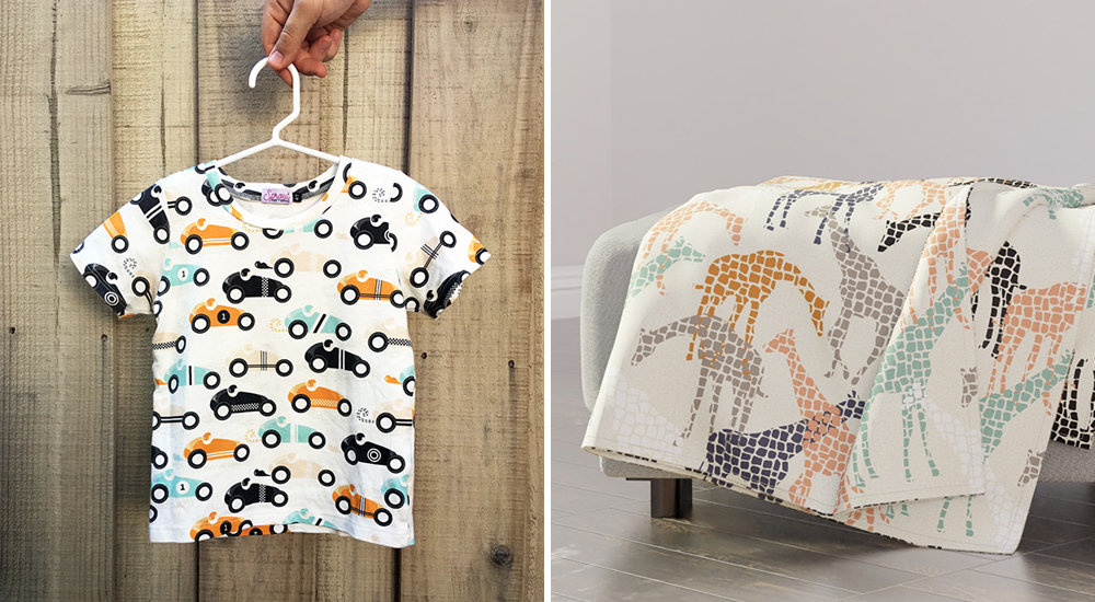 A small shirt with cream and orange and black and sage racecars on a white background. The shirt is hung on a white hanger against a wooden slat fence. On the right, a cloth with giraffes in orange and brown and sage and peach on a cream background. They are both Daniel's designs. 