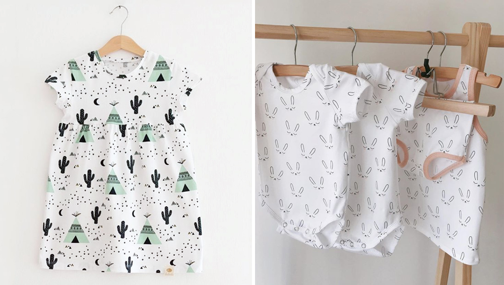 On the left: Claudia's design Teepee on a white background is shown on an small white dress. The design has a mint green teepee repeating in a desert with a black cactus and moon. 
On the right: Claudia's design Sleepy Bunny on several small one-piece rompers hanging on a wooden rail. The design features a repeating sleeping bunny with closed black eyes, a round black nose and two ears outlined in black.
