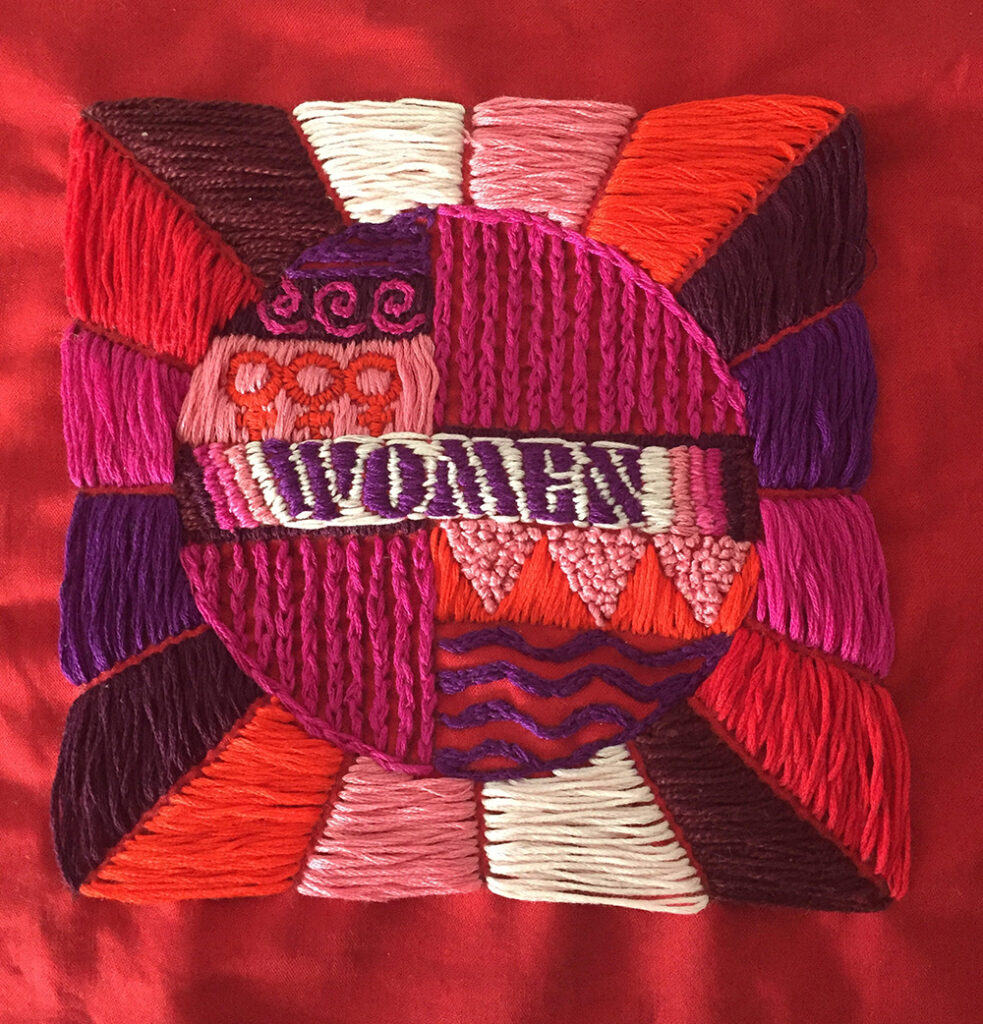 An embroidery design by Alyson in celebration of International Women's Day. The design has the word "Women" stitched in the middle in purple on a white background. Pink, red and cream geometric designs encircle the word "women" in thread. 
