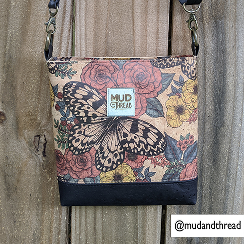 One of Katerina's designs is on a bag by Mud Thread. The design has a light brown background, and black-and-white butterfly with red and yellow flowers with green leaves behind it. 