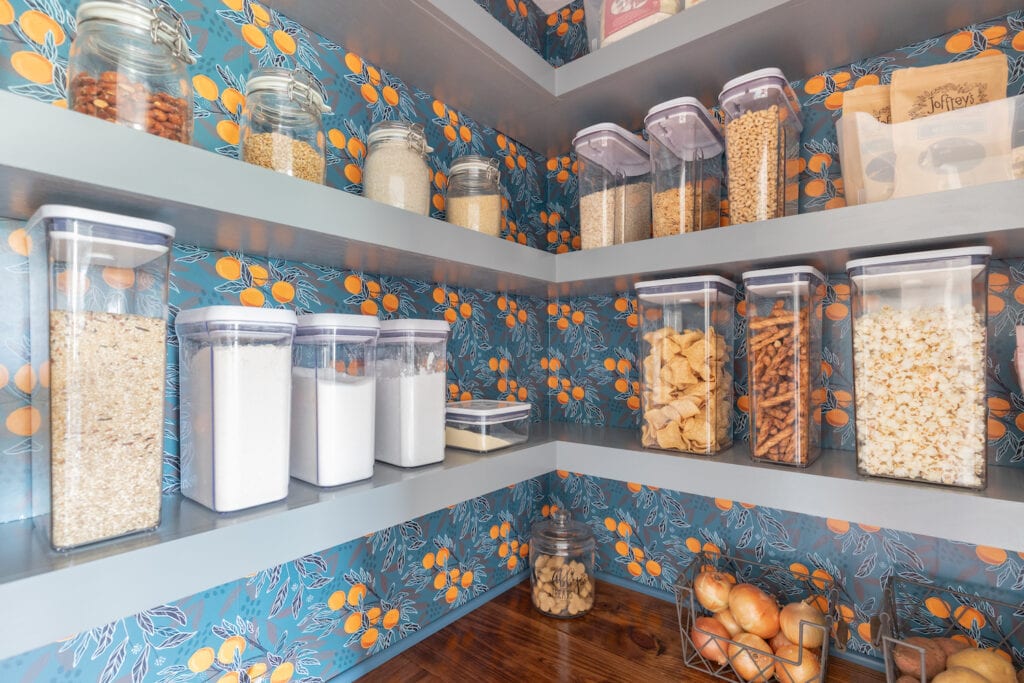 A kitchen wall with shelving uses a bold green blue patterned wallpaper