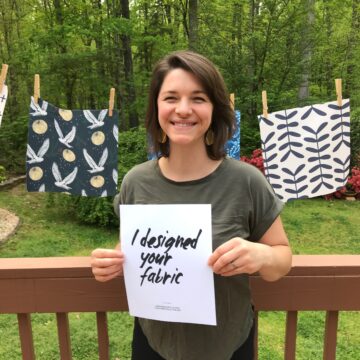 Katie stands in front of a clotheslines with her fabric swatches holding a sign that says 