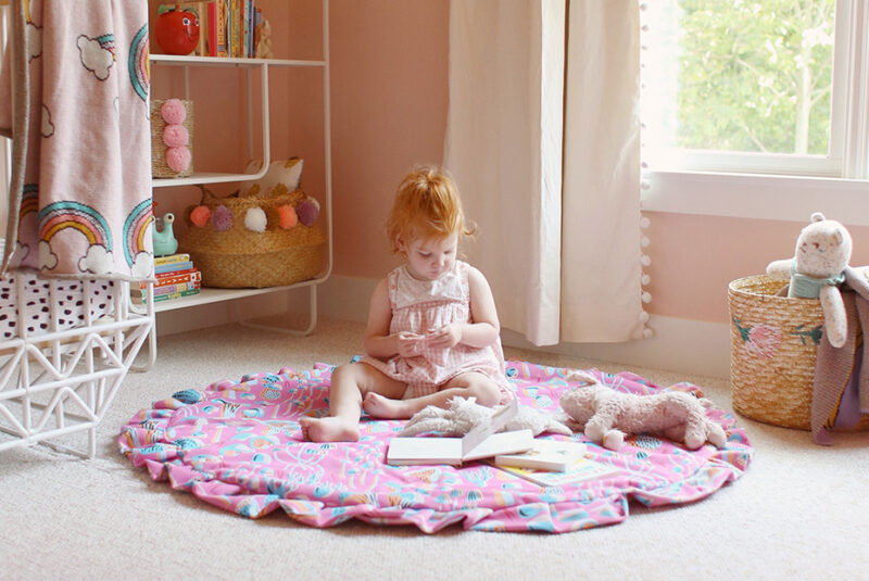 Toddler sitting on a pink playmat in playroom