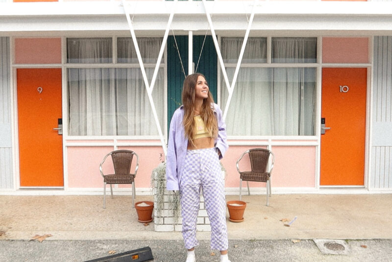Maddy wears purple and white checkered pants in front of a retro building
