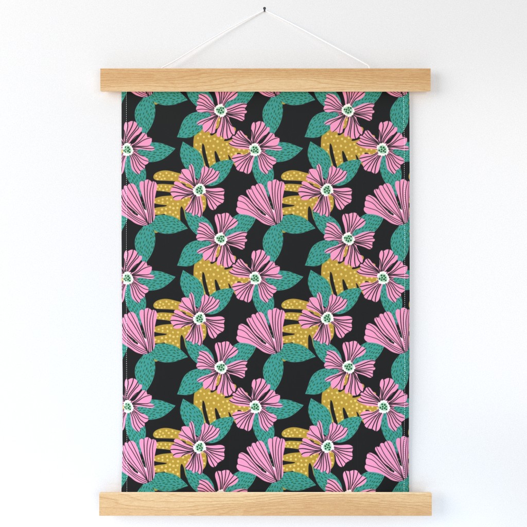 A wall hanging featuring tropical pink flowers with green and gold polka dot leaves on a black background hangs on a white wall