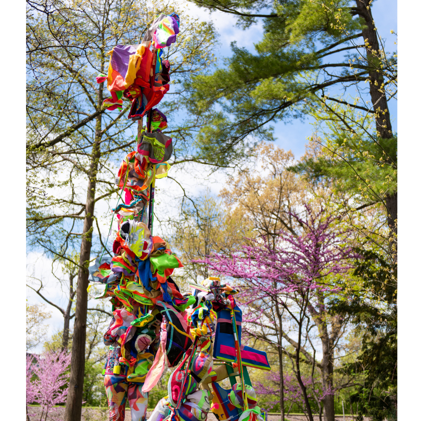 A tall brightly colored sculpture by Lindsey Whittle stands amongst trees.