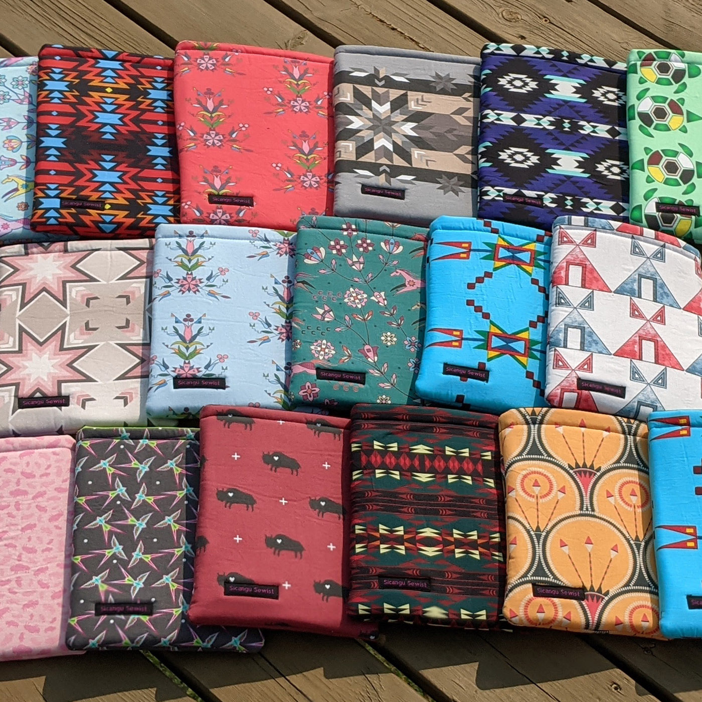 A group of handmade book sleeves created by Lorna "Emmy" Her Many Horses in a range of colors featuring some designs by the Indigenous artists featured in this blog post. Select styles are available on Emmy’s Etsy shop, The Sičángu Sewist.