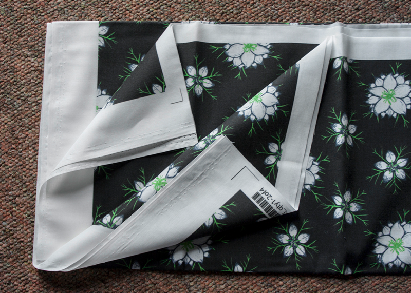 Vicky's fabric of small white flowers with large petals in the innermost part with a green wispy center and smaller petals around the outer edges on a black background. 