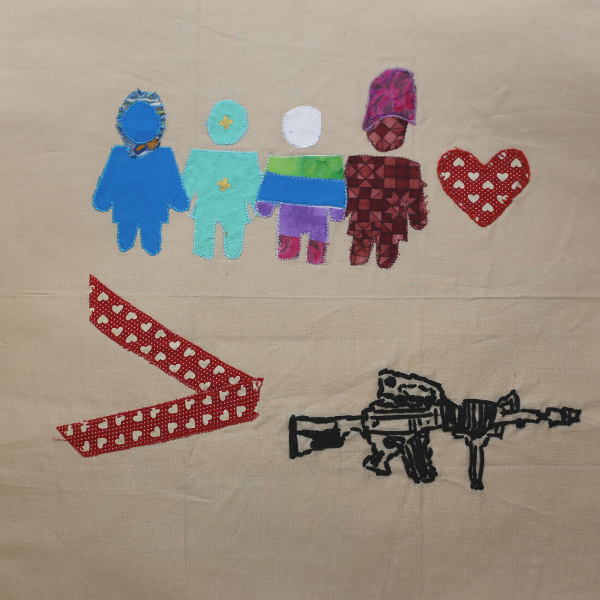 A quilt block with a light brown background and two rows of small quilted images. On the top row are four faceless figures, one with bright blue shirt, pants and face and a shiny blue headscarf. One figure is turquoise from head to toe, with a gold dot where the person’s face would be and a gold dot on the center of their chest. The third figure has an all white head, they are wearing clothes with thick stripes in the following colors, green, blue, purple and magenta. The last figure in the row has a light brown and dark brown checkered body and face. They are wearing a magenta hat on their head. To their right is a large red heart made out of fabric that has rows of small white hearts on it. On the bottom row, there is a sideways V, with the open side pointing to the left and the closed side pointing to the right, in the same red fabric with small red hearts. A black machine gun is pointing to the right and is to the right of the sideways V.