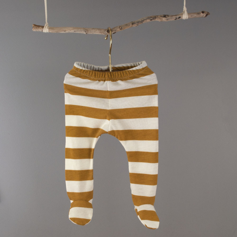 Small white and light brown footie leggings hang on a branch against a dark gray background.