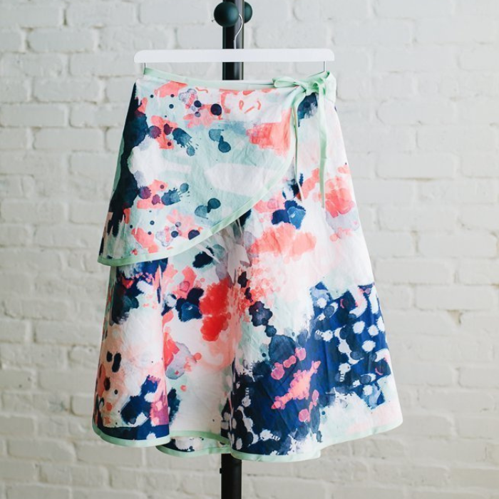 A floral wrap skirt with a white background navy, green and pink accents hangs on a hanger