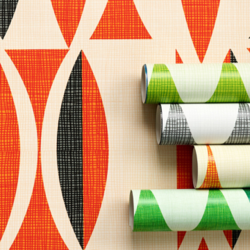 A panel of wallpaper with repeating rows of narrow ovals with pointed tops and bottoms on a cream background is shown laying as if installed on a wall it is taking up the entire background of the image. The ovals are randomly black and dark orange. In the middle third on the right-hand side of the image, four rolls of the same wallpaper design in different colorways are laid lengthwise on top of the black-and-dark-orange panel. Only about a fourth of the rolls are shown. The rolls of wallpaper from top to bottom feature green-and-blue ovals on a cream background, black-and-white ovals on a cream background, orange-and-gray ovals on a cream background and kelly-green-and-dark-green ovals on a cream background.