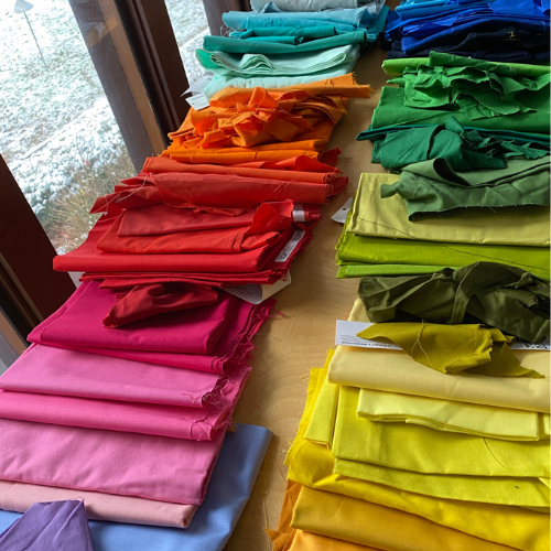 Dozens of small folded pieces of fabric are laid out by hue on a wooden table.
