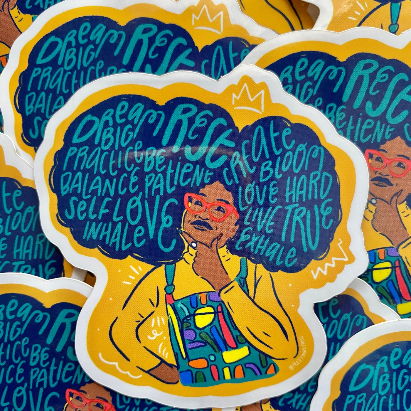 A stack of stickers of a person with their left hand to their chin and their right hand to their hip. A word cloud shows words like dream, big, practice, self love, inhale and more in light blue in the person's large navy blue hair.