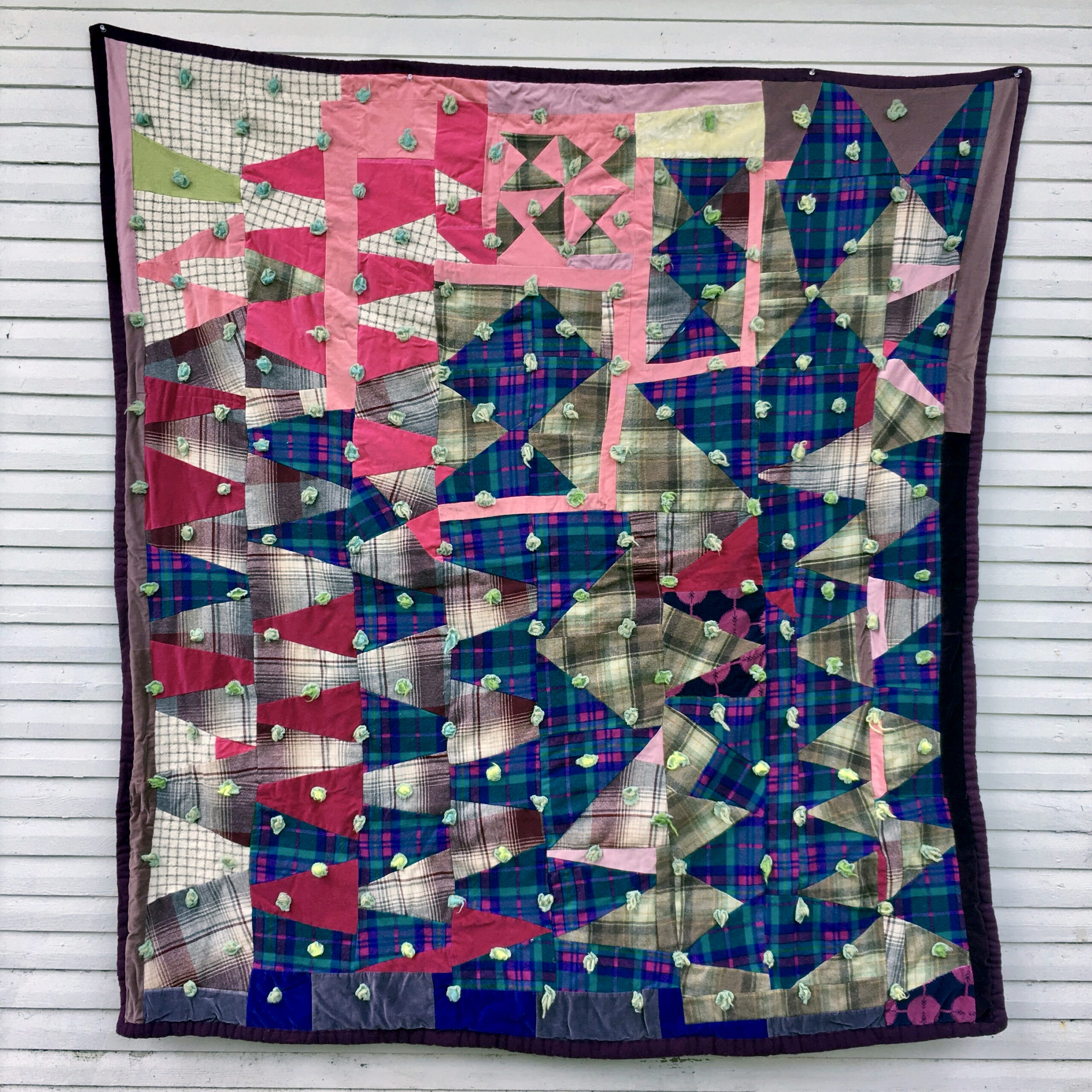 A quilt made of vertical rows of small triangles pieced together, some are pink, some are blue, some are white, some are plaids comprised of neutral colors.