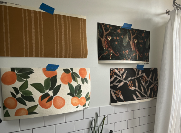 Bathroom with white walls and white subway tile. On the wall hang four wallpaper swatches featuring orange citrus, mustard and white stripes, tigers and peacocks, and black and gold floral patterns.