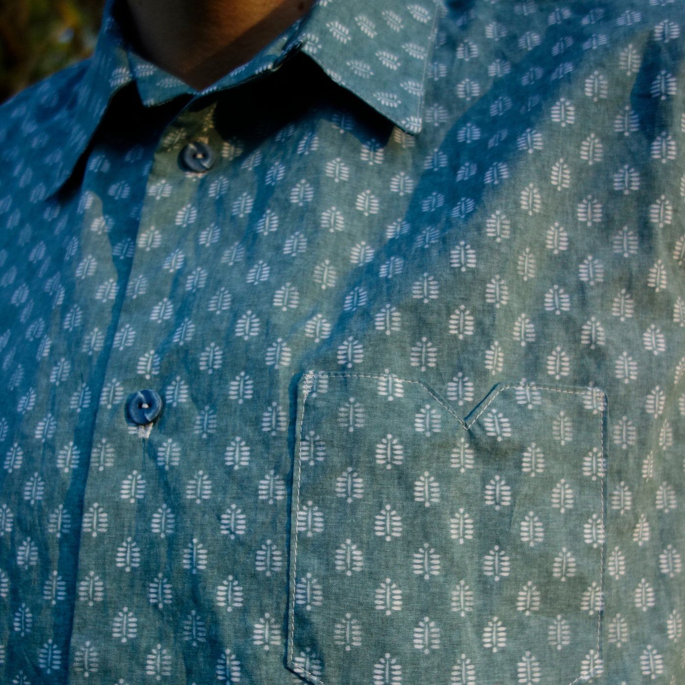 A close up of the neck and pocket at the top of a button-up shirt. The shirt has repeating rows of small white block print ferns.