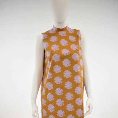 A mannequin wears an orange dress with repeating rows of lavender floral-like bursts in front of a white background.