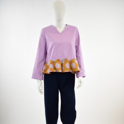 A mannequin wears a lavender shirt with an orange ruffle at the bottom with repeating rows of pink floral-like bursts and dark blue pants in front of a white background.