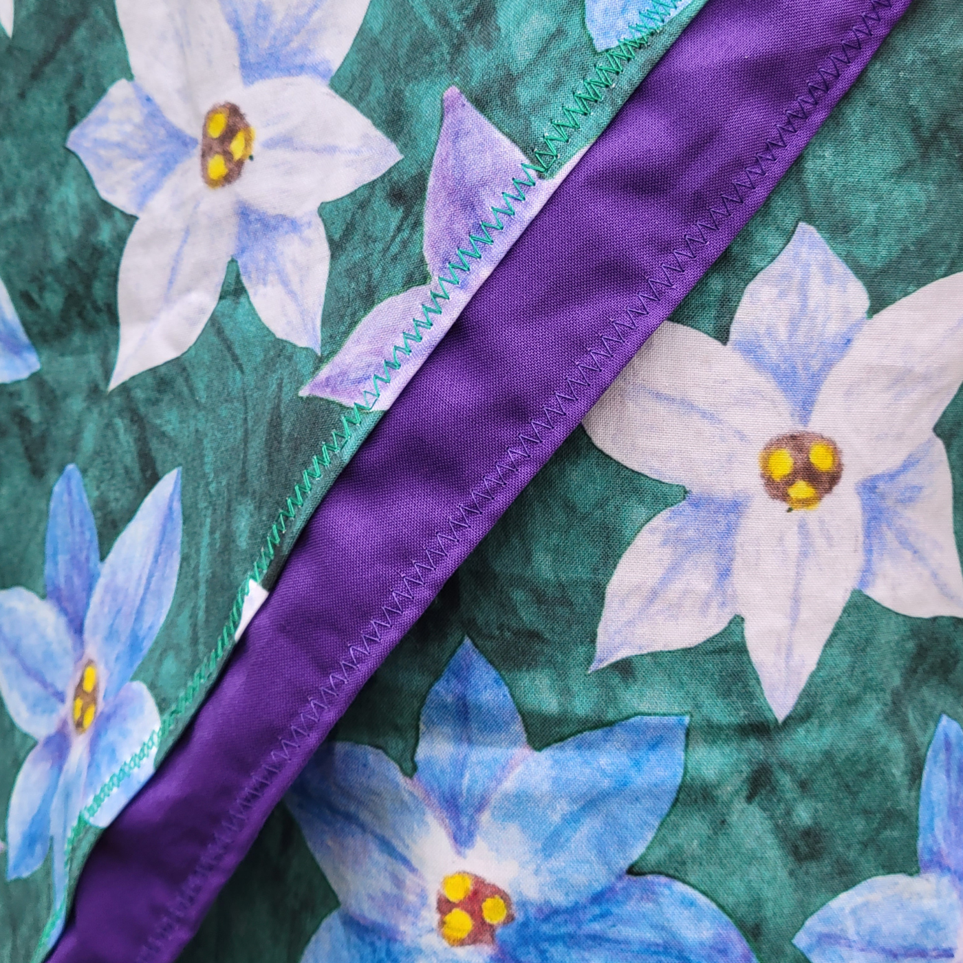 A close up of a wrap skirt featuring a design with large purple, white and blue starflowers. The skirt has a strip of purple fabric on the wrapped section part of the fabric, which goes diagonally down the front of the skirt.