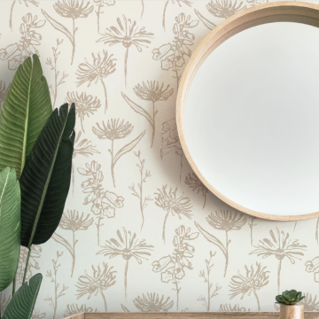 A screenshot of a wallpaper render of @h_u_f_t_o_n’s Fall Blooms design as shared on Instagram. The image features a wall with a wallpaper design with a cream background and repeating light brown hand drawn flowers. A round mirror is at the top of the image with the top of a light wood table just at the bottom of the frame. A small succulent in a small wooden planter is on top of the table. Leaves of a green plant are peeking into the left edge of the image.