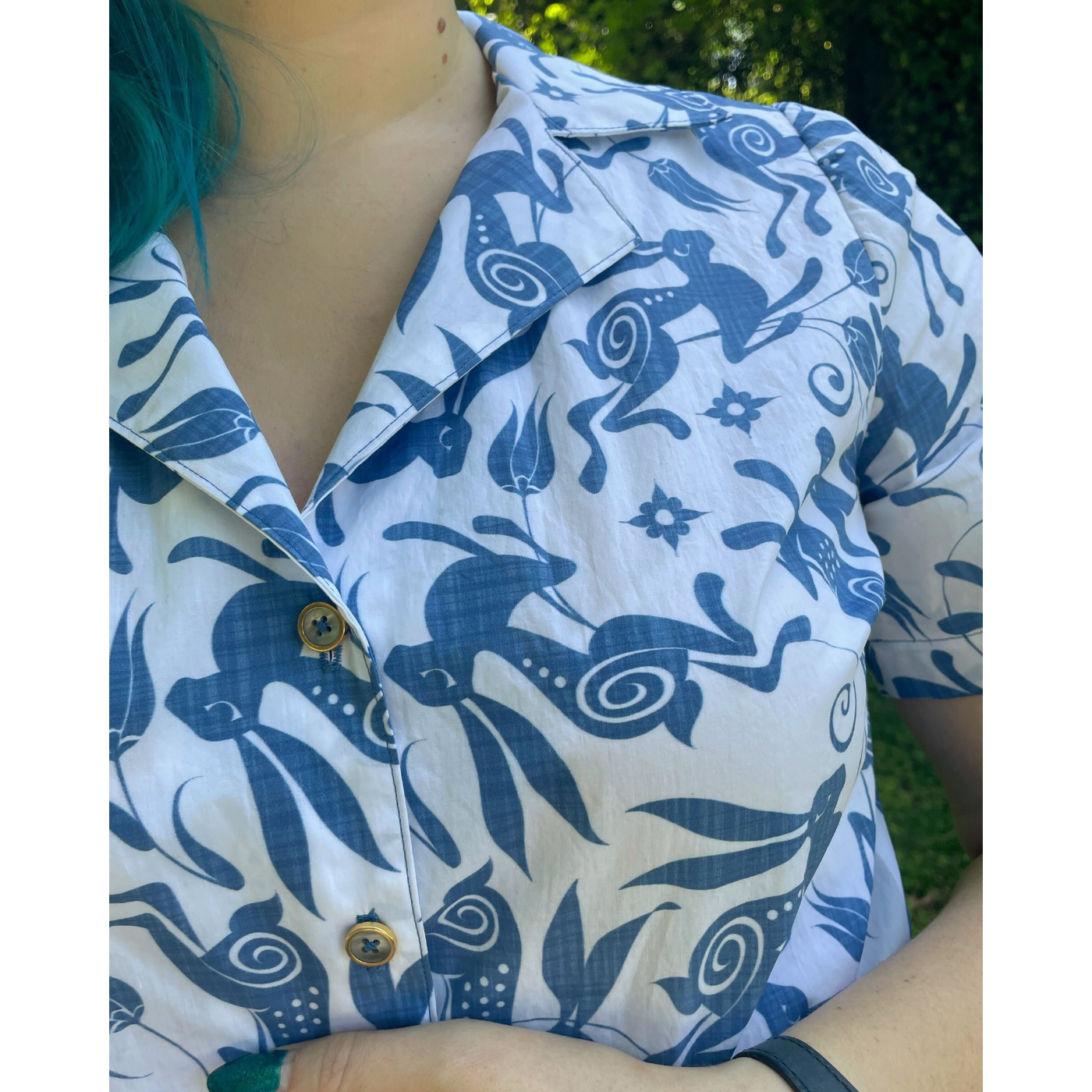 A close up of the top of a white short-sleeve shirt with buttons up the front featuring a design with blue bunnies and blue tulips floating through it.