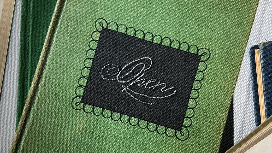 A green fabric book cover with a black rectangle patch. The patch has "Open" in cursive embroidery written