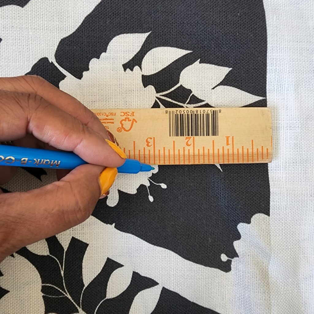 Tracey marks one edge of the border with a blue water-soluble pen. A ruler is at the top of the photo, she is marking the border at the 3” (2.54 cm) mark. 