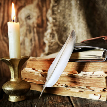 A candle, feather with ink and a stack of books.