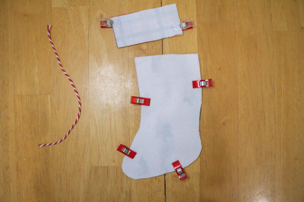 Two fabric pieces for the stocking cuff and two fabric pieces for the stocking boot have been cut out of the fabric. The two pieces for the cuff are clipped together with the right sides together (i.e. with the white backing of the fabric showing). The same thing has been done for the boot.