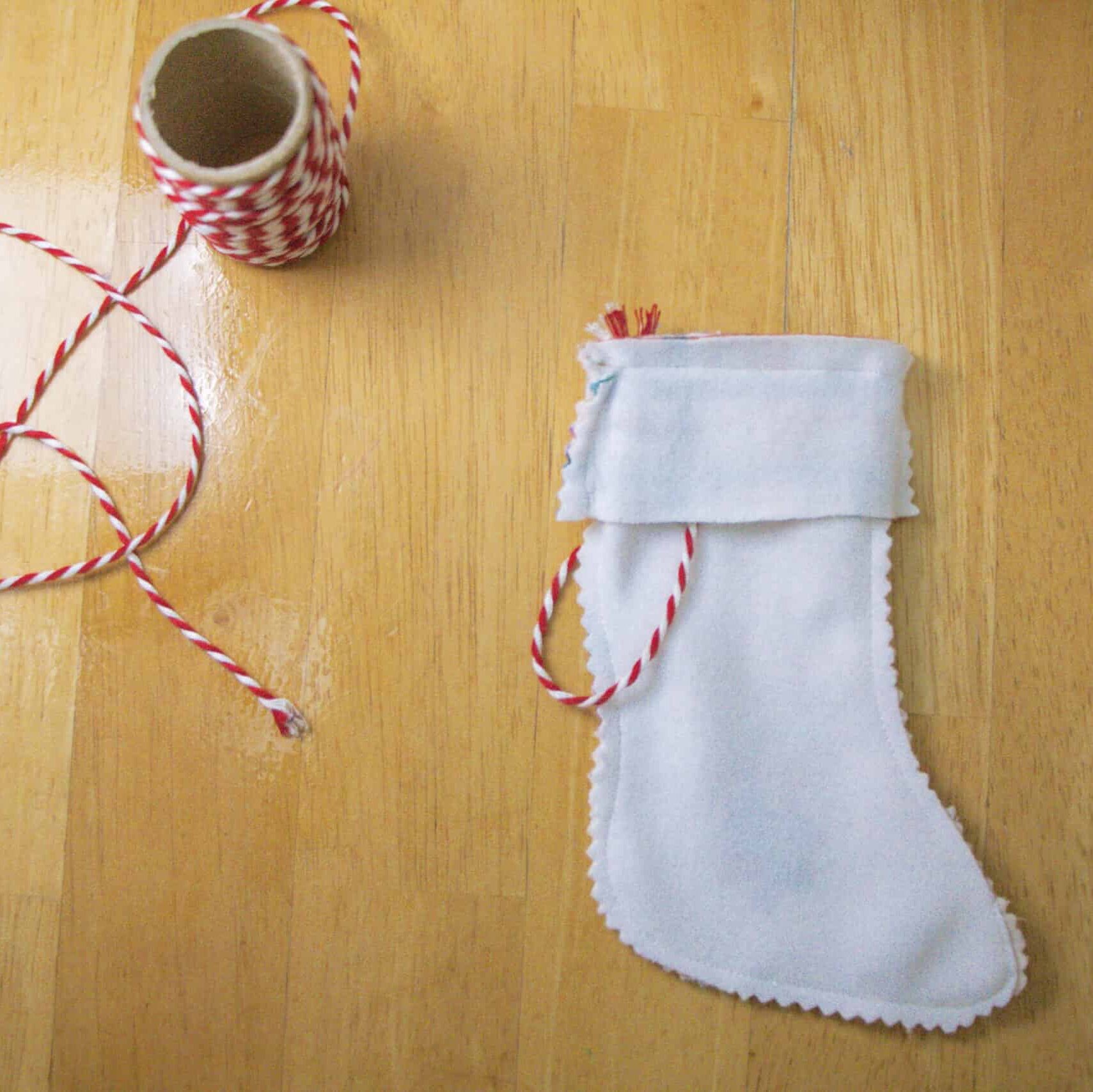 Image of the stocking after sewing around the top edge. It is still turned inside out with the white “wrong” sides of the fabric showing. The top seam has been sewn with a light blue thread. 