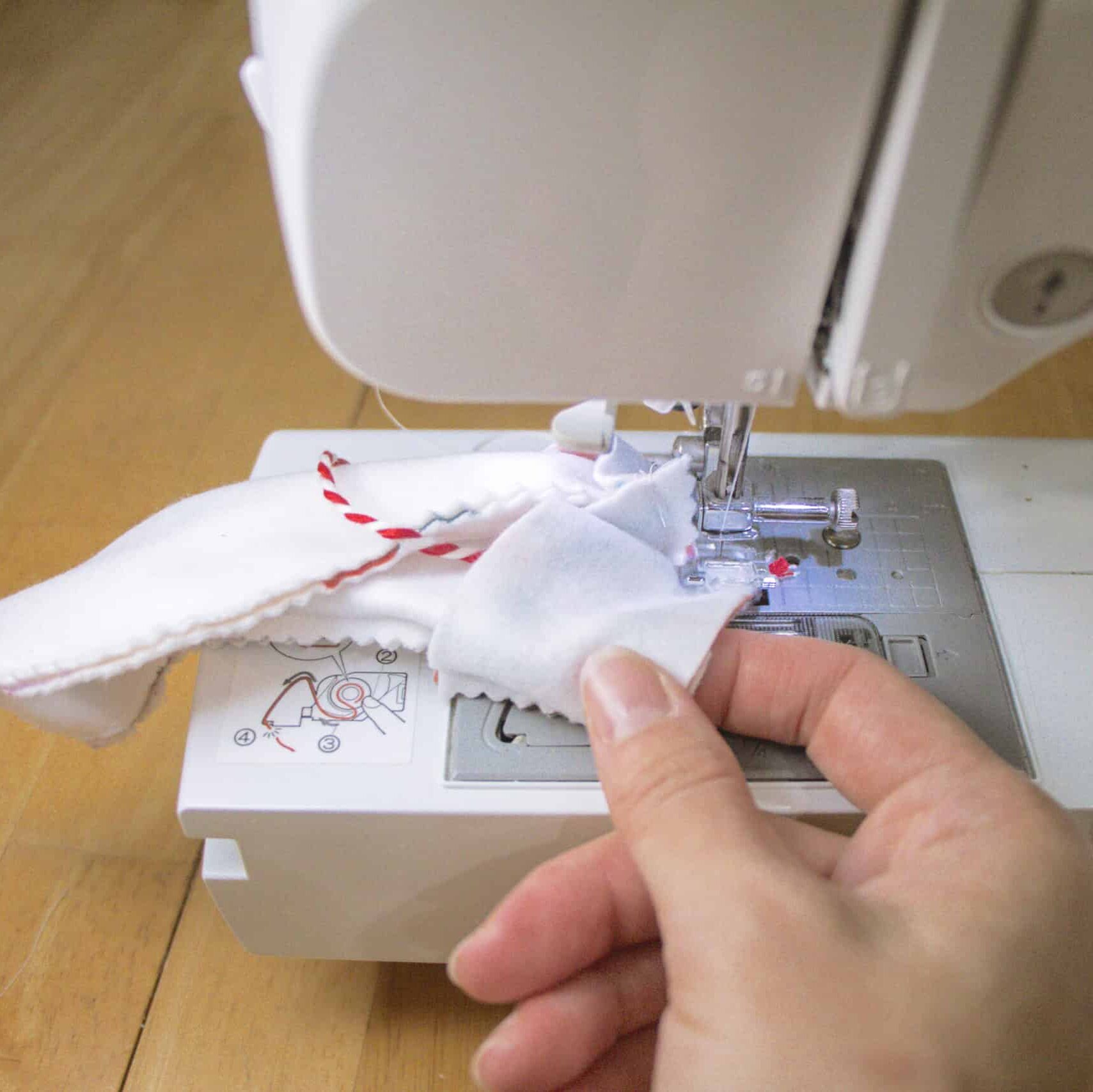 A hand guides the sewing machine carefully as it sews around the top of the stocking,