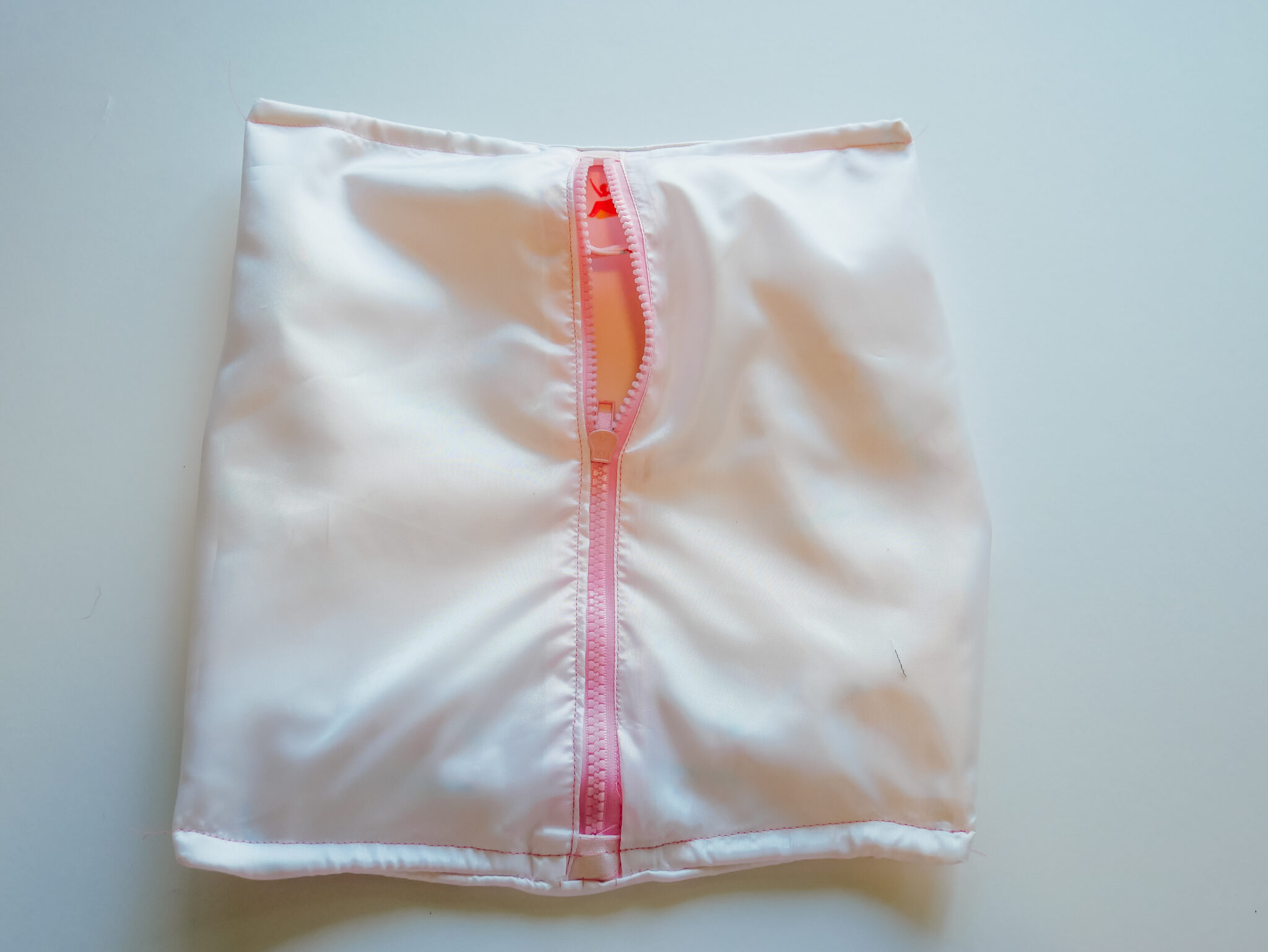 A rectangle-shaped bag has been turned inside out, the Polyurethane Laminate fabric is showing as is the back side of a pink zipper. The bag is laying on a white surface.