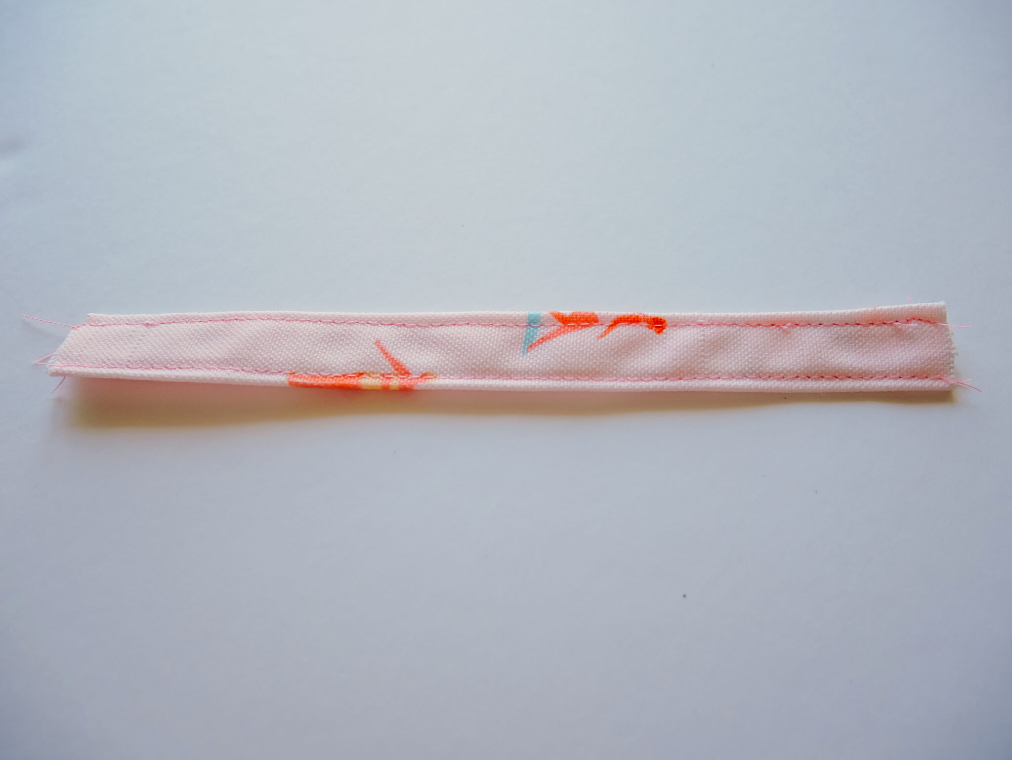 A small rectangle of fabric has been sewn along the top edge and the bottom edge. The fabric features a design with small female surfers surfing through a pink background.