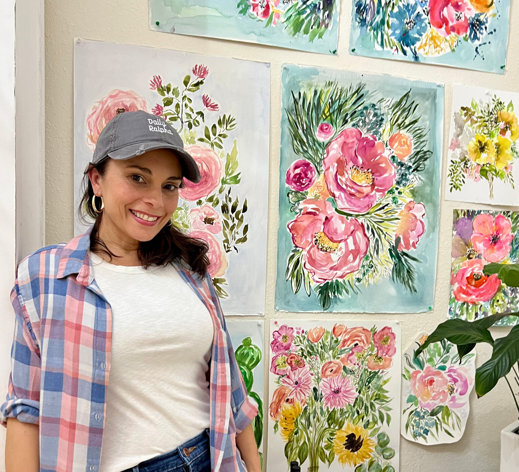 Spoonflower Artist Judy Quintero stands in front of a wall with nine hand painted florals pinned up in a variety of soft colors.
