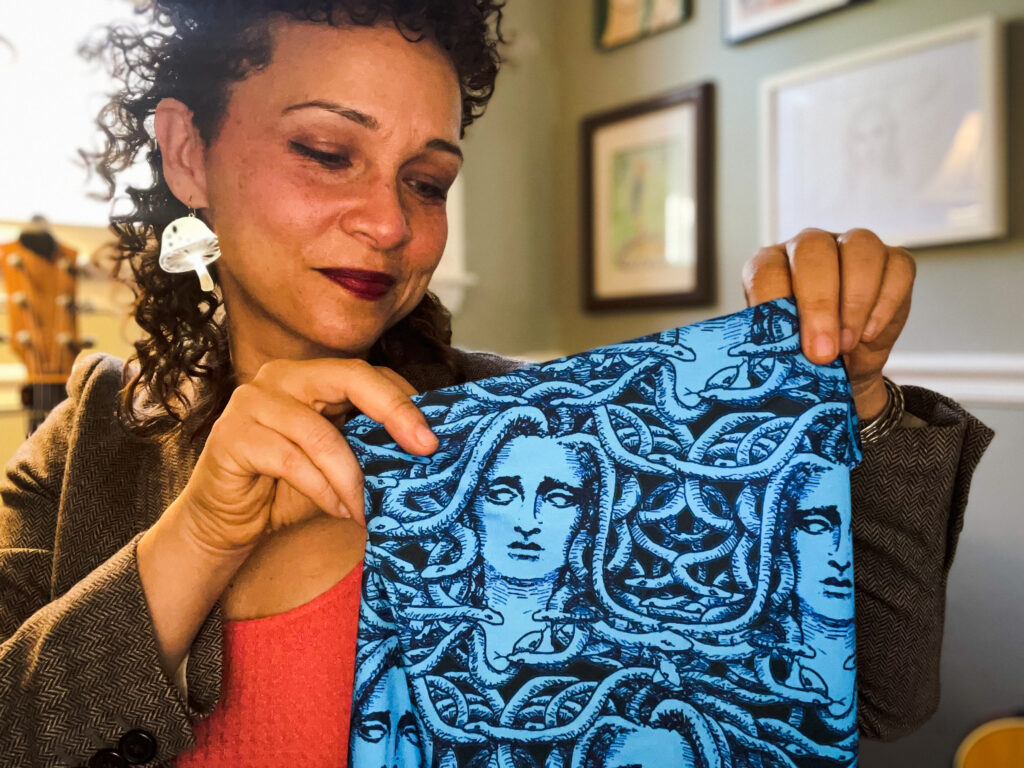 Jennifer holds up heatherinbrooklyn’s Medusa Small design printed on Modern Jersey fabric. She is looking at the fabric, which is bright blue and features a repeat drawing of Medusa with black in details.