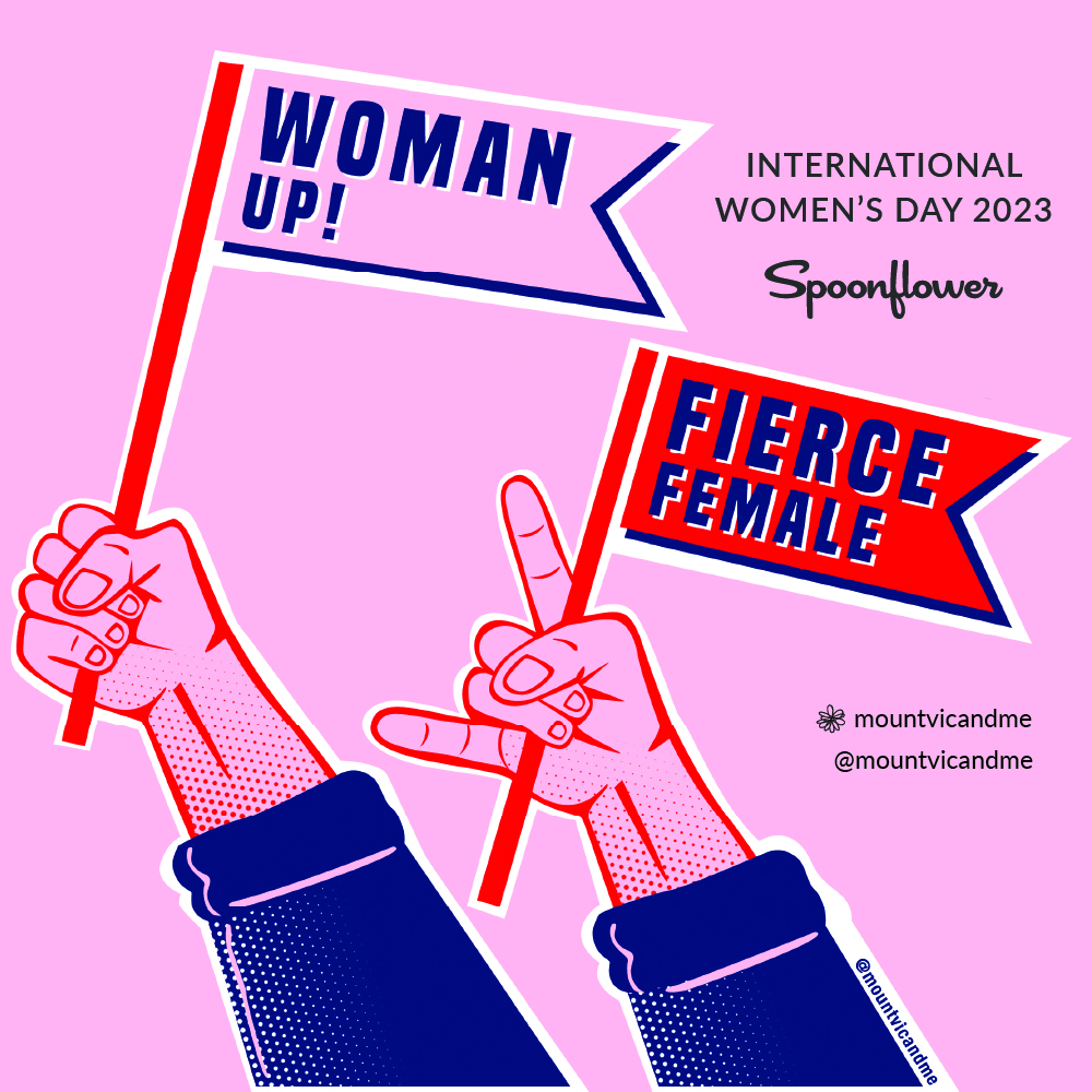 A sticker by Kara Cooper for International Women’s Day. At top right is the text International Women’s Day 2023, Spoonflower. In the middle right right, in black font is Kara's Instagram handle and Spoonflower shop name, mountvicandme. The design has a pink background and two hands holding small flags. One flag is pink and says “Woman Up!” in dark blue. The other flag is red and says “Fierce Female” in dark blue.