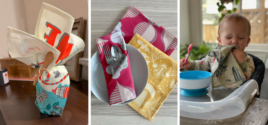 Three photos are side by side. On the left, a tea towel with a vintage Maine design has been used to wrap a gift that is sitting on a wooden table. A small wooden spoon is tied around the top of the gift with white twine. In the middle, a folded napkin sit on top of a white ceramic bowl with a silver fork and spoon tucked inside. Two napkins lay tesselated underneath the bowl. The napkin folded on the bowl and the napkin laying directly against the table have a deep magenta background and repeating design with beets in a half drop repeat that are pink on one half, pink, magenta and gray striped on the other half and have gray tops. The napkin directly underneath the bowl has a deep yellow background and cream-colored mushrooms and small leaves. The bowl and napkins are lying on a light wooden table. And on the right, a small child in a high chair uses a cloth dinner napkin to wipe off food. In the child’s left hand is a small red plastic spoon. In its right hand, is a napkin with a design featuring a woodland alien abduction. A blue-and-white bowl sits on the highchair’s table top.