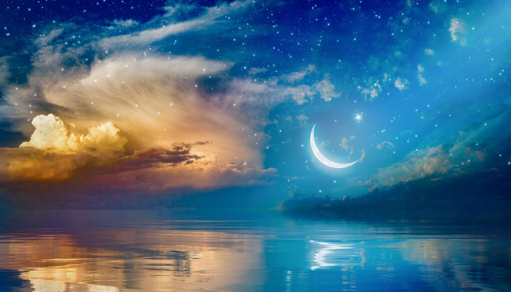 A peaceful enhanced photo of the ocean at night with twinkling stars, a sliver of the moon, and yellow clouds reflecting in the blue water.