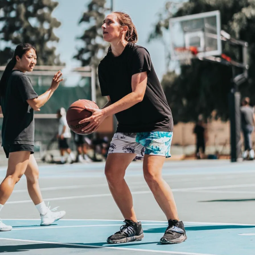 A woman is on a basketball court with a basketball in her hands, getting ready to shoot. She wears shorts that are white on one side and blue on the other.