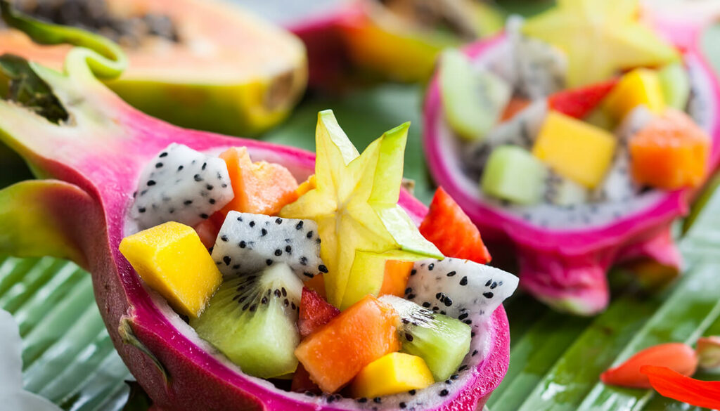 Hollowed out pink dragonfruit hold a delicious assortment of tropical fruit including kiwi, mango, strawberry and papaya, topped with a slice of star fruit.