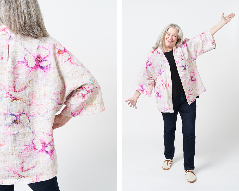 Two photos have been placed side by side in a rectangle. On the left, a close up of the back of Sue’s robe jacket. On the right, Sue smiles at looks at the camera with her hands held out to her sides and wearing her robe jacket with black pants and a black top underneath it. She is standing in front of a white background. The design on her robe jacket features magenta, orange and blue magnolia blossoms on a white background.