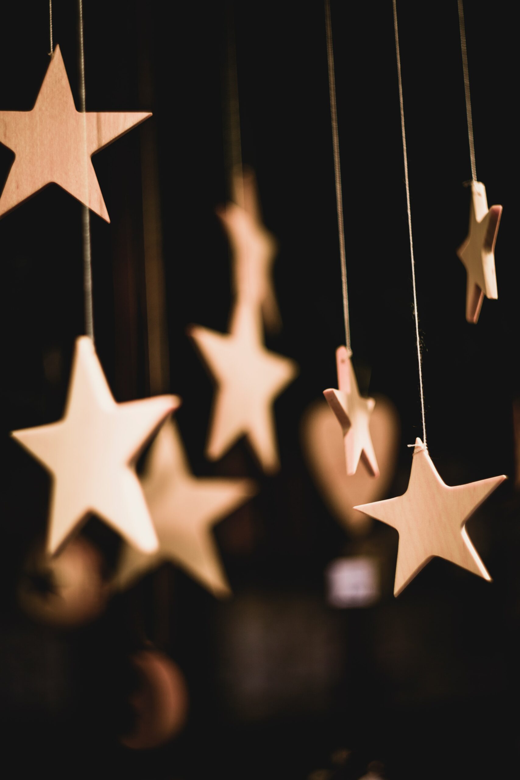 Light brown wooden stars hang on fishing line against a black background and are shown from slightly below.